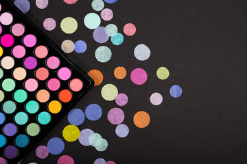 Colorful make-up palette with colorful confetti scattered on black background