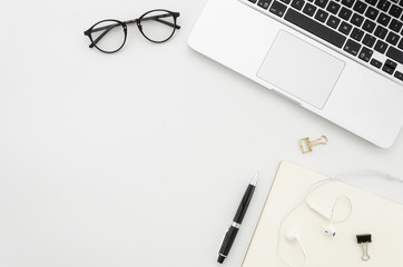 Modern minimalistic work place. White office desk table with laptop, clips, glasses, notebook, pen and headphones. Top view with copy space, flat lay mock up