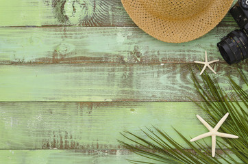 Freelance concept summer hat, camera, seastars and paln leaf on green wooden background Top View Close-up flat lay