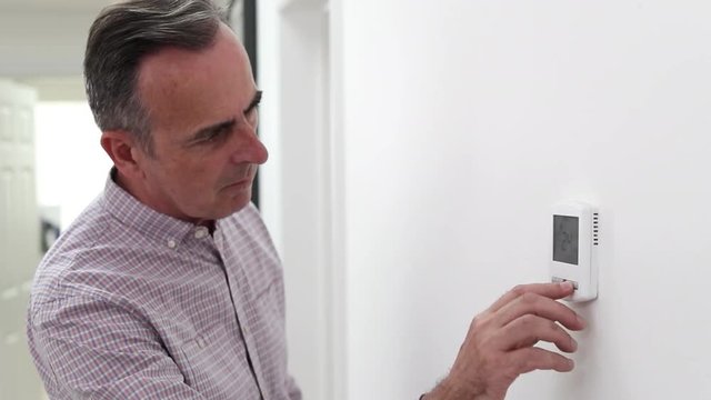 Man Adjusting Central Heating Thermostat At Home