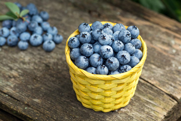 Wicker yellow basket with blueberries on a wooden table in the garden