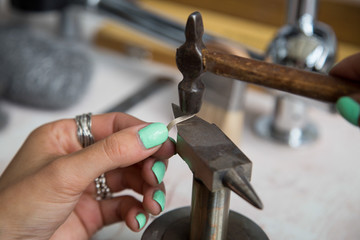 The process of making silver jewellery. Hammering the silver ring. Female artist hands close up....