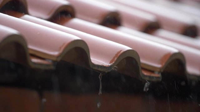 Heavy rain falls on terracotta roof tiles - filmed in slow motion.