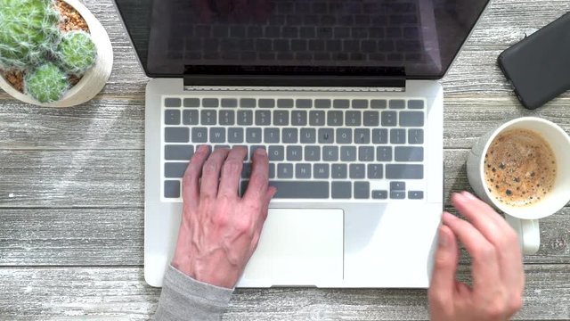 Person typing on laptop computer and drinking coffee on a wooden desk