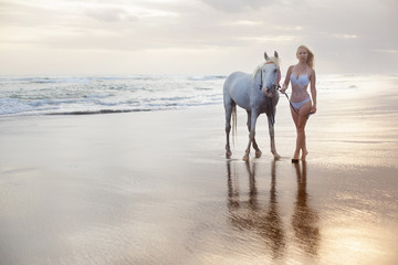 Beautiful young woman walking with horse at the beach, horseback