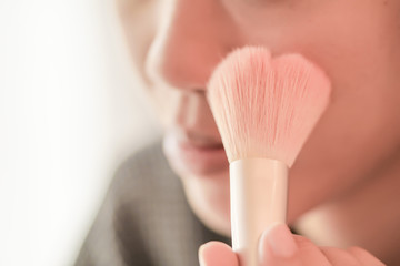 Pretty girl is applying blush on cheek by brush.
