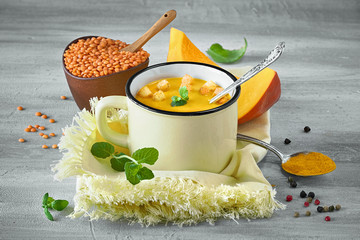 Tasty pumpkin cream soup served with croutons in light yellow mug on matching napkin. Carved...