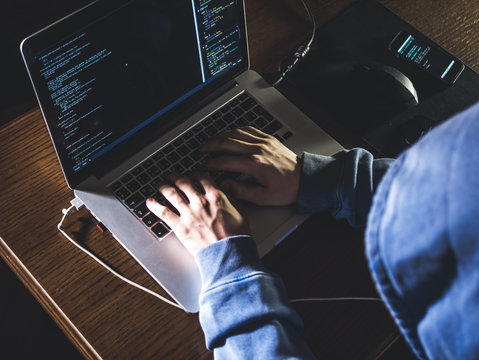 overhead hacker in the hood working with laptop and mobile phone typing text in dark room