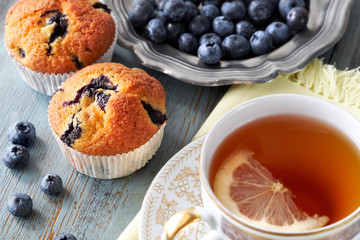 Close-up on blueberry muffin and cup of tea with lemon on gray rustic wood