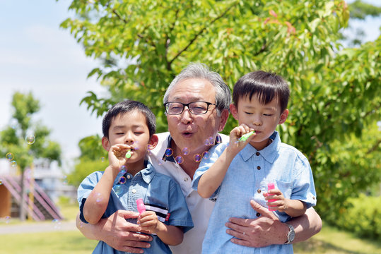 公園でシャボン玉を楽しむ孫を抱きしめるシニア男性