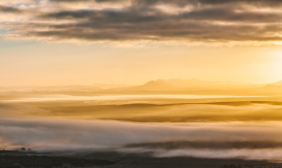Beautiful glowing sunrise landscape - clouds laying low covering mountain silhouettes