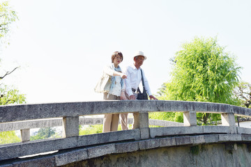 旅先の観光地の橋の上で、川を指さすシニア夫婦