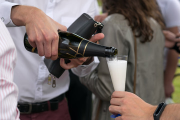 the hand of the man in the white shirt pours champagne on a holiday in the open air