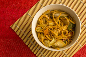 Fried noodle.  Yakisoba with beef, ticken and vegetables in a white bowl on a red background. Asian cuisine meal.