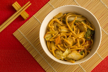 Fried noodle.  Yakisoba with beef, ticken and vegetables in a white bowl on a red background. Asian cuisine meal.