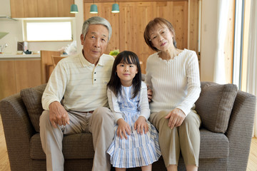 リビングのソファで微笑むシニア夫婦と孫娘