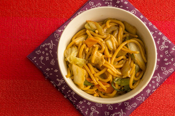 Fried noodle.  Yakisoba with beef, ticken and vegetables in a white bowl on a red background. Asian cuisine meal.