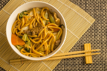 Fried noodle.  Yakisoba with beef, ticken and vegetables in a white bowl on a dark background. Asian cuisine meal.