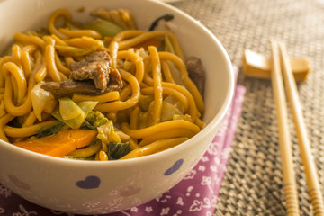 Fried noodle.  Yakisoba with beef, ticken and vegetables in a white bowl on a dark background. Asian cuisine meal.