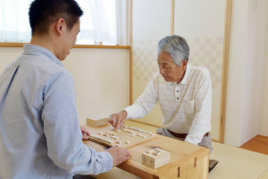 和室で将棋を楽しむシニア男性と若い男性