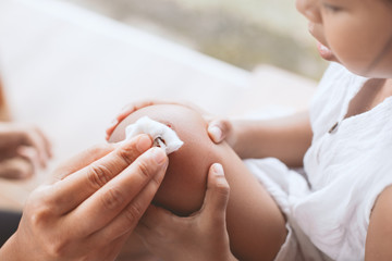 Parent helping her child perform first aid knee injury after she has been an accident