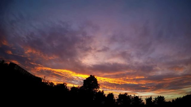A colorful sunset over the shrubs and a house on the left. Timelapse