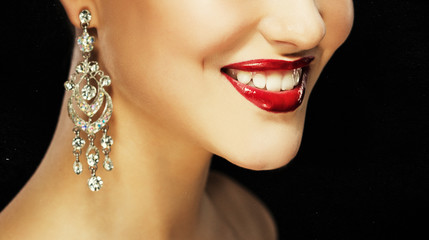 Beautiful brunette woman with bright make-up and jewelry earrings smiling close-up. Red lips and nails, evening make-up