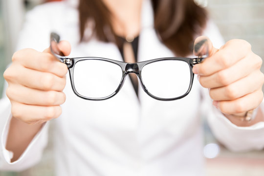 Woman optician holding black frame eyeglasses in hand