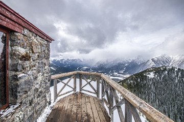 Wide angle view on top of a mountain looking over the wooden railing at the mountain view. It was a cloudy and cold winter day at Banff National Park.