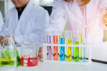 Hand of Scientist woman holding dropper and row of colorful test tube in a laboratory. Concept chemistry medical image.