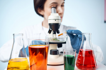Multicolored liquids in flasks and a laboratory assistant with a microscope