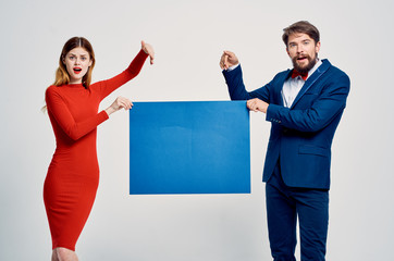 woman in red dress and man in suit show hand on blue sheet of paper