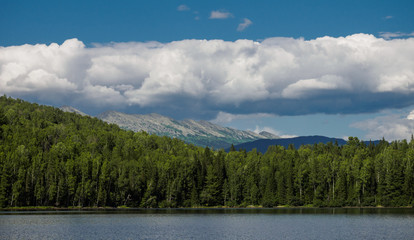 panorama of the forest on the lake behind which you can see the mountains over which stretched long white clouds