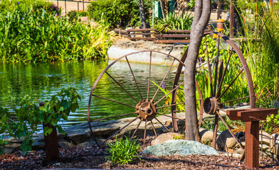 Two Rusty Metal Wheels In Planter Area Next To Pond