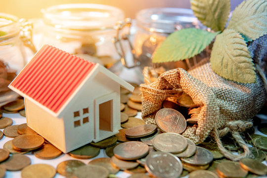 Property or real estate investment. Home mortgage loan rate. Saving money for future concept. House model with gold coins in currency glass jar and spilling out of money bag on the table