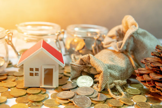 Property or real estate investment. Home mortgage loan rate. Saving money for future concept. House model with gold coins in currency glass jar and spilling out of money bag on the table