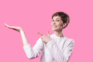Excited girl pointing showing at pink background with copy space. Young beautiful happy smiling and laughing woman