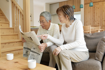 リビングのソファで新聞を読むシニア夫婦