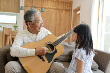 リビングのソファで孫娘とギターを弾くシニア男性