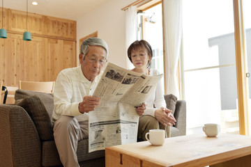 リビングのソファで新聞を読むシニア夫婦
