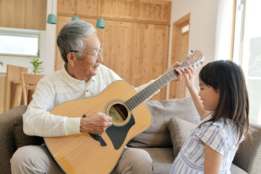 リビングのソファで孫娘とギターを弾くシニア男性