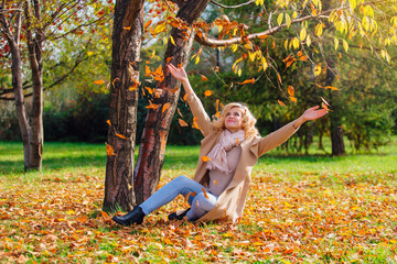 Young beautiful woman throwing up fallen autumn leaves over her head