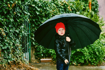 a boy walks on the street with a black umbrella