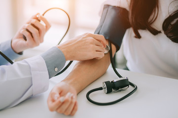 Doctor using sphygmomanometer with stethoscope checking blood pressure to a patient in the hospital.