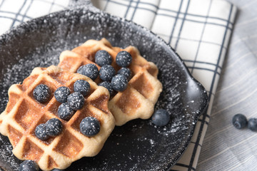 Belgium waffle with blueberry topping in the pan on the tablecloth