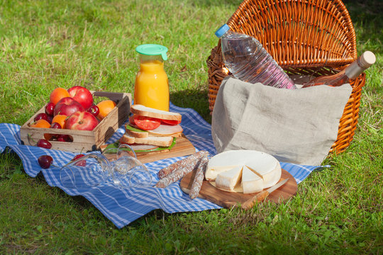 Picnic basket with different snacks on the green grass in the garden