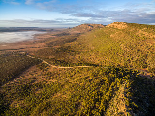 Winding road below rugged cliffs and low morning clouds at sunrise. Jarvis Hill lookout, Hawker, South Australia