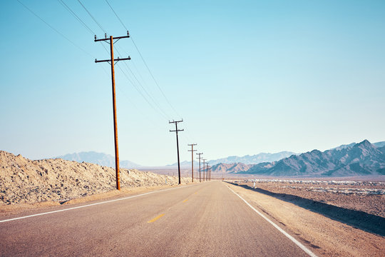 Desert road with wooden electricity posts, color toned picture, USA.