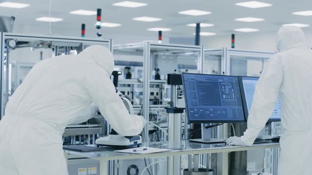 In Laboratory Scientists in Protective Clothes Doing Research, Using Microscope and Entering Data into Personal Computer.  Shot on RED EPIC-W 8K.