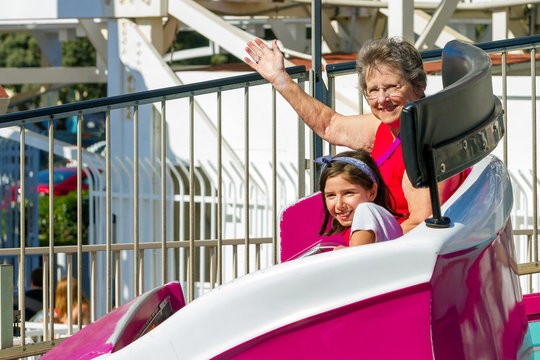 Elderly Woman Rides On A Tilting Spinning Ride At A Theme Park With Her Young Granddaughter